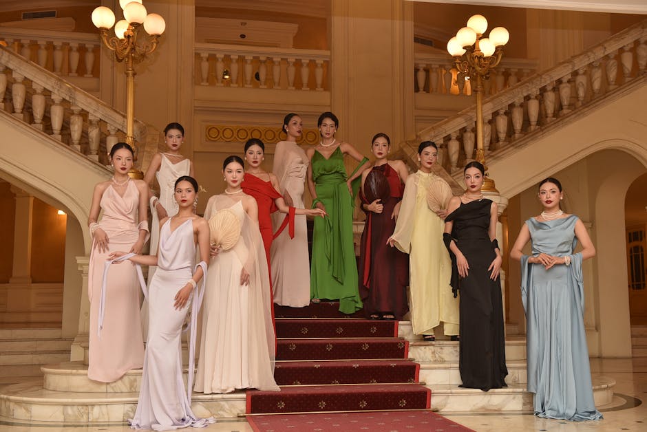 Group of diverse fashion models posing in elegant evening gowns on luxurious staircase indoors