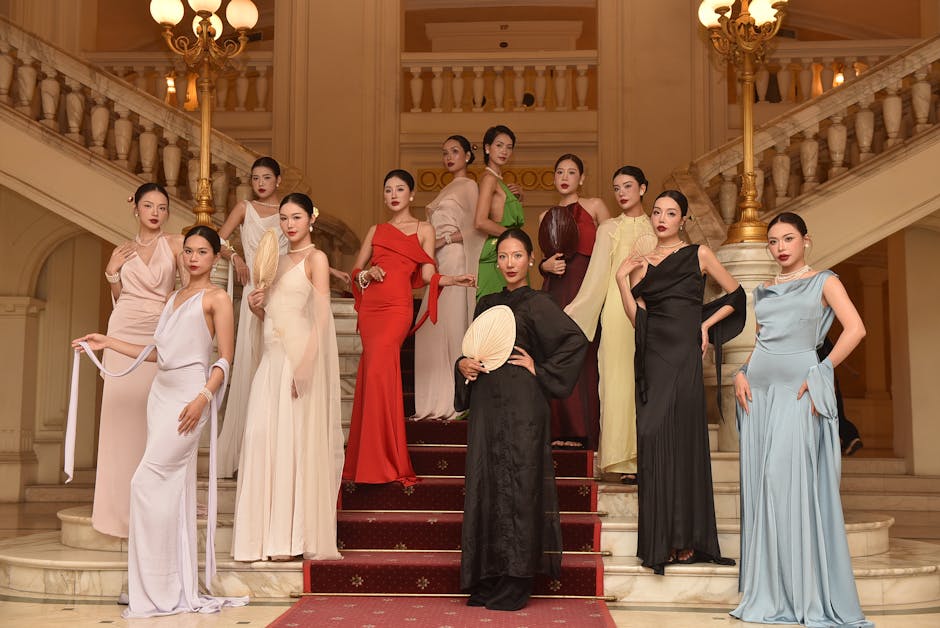 A group of fashion models in elegant gowns posed on a grand staircase indoors
